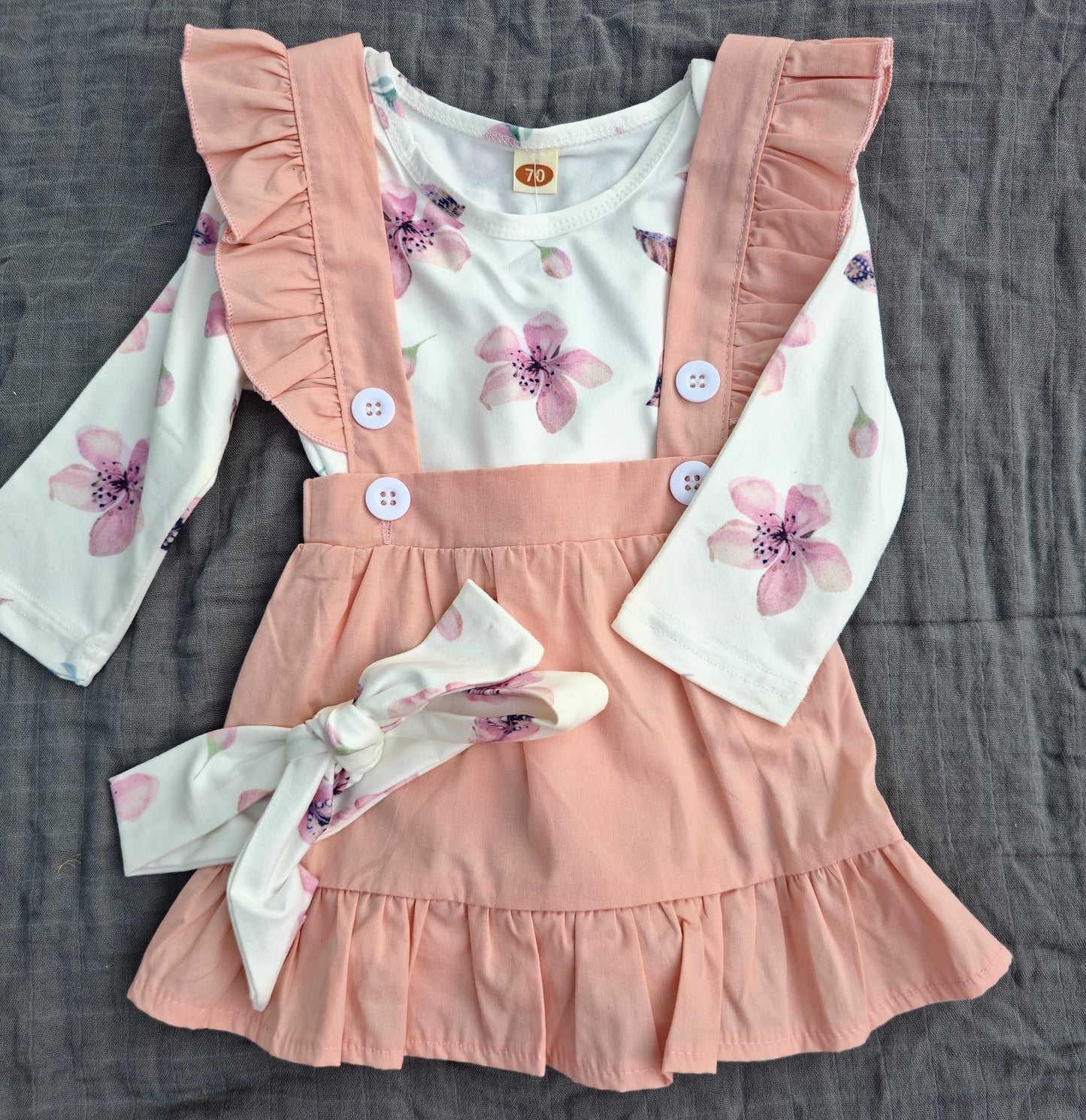 Children's outfit with pink ruffled overalls and floral top on a gray surface