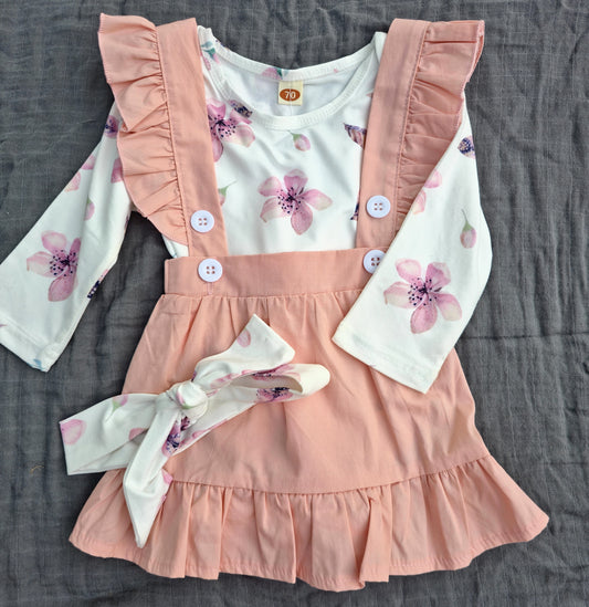 Children's outfit with pink ruffled overalls and floral top on a gray surface